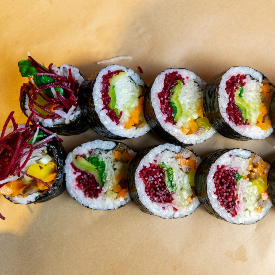 Close-up of GimMeBap's colorful Korean gimbap rolls with various fillings on a brown surface.