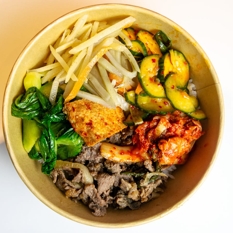 A close-up of a GimMeBap Korean bibimbap bowl with beef, kimchi, and various vegetables.